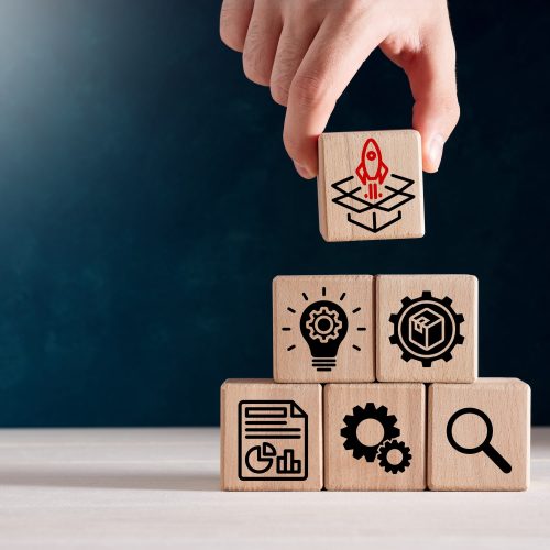 Product development, launching, analysis and market validation. MVP, minimum viable product concept for lean startup. Hand puts wooden cubes with new product launch icons.